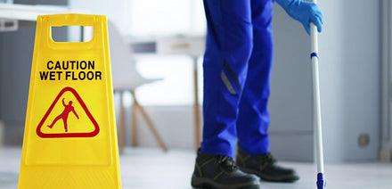 Professional cleaner mopping a floor next to a yellow wet floor sign in a commercial building