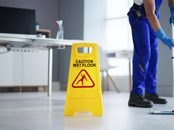 Professional cleaner mopping a floor next to a yellow wet floor sign in a commercial building